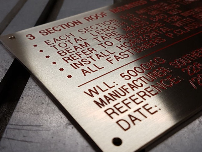 engraved brass plaque with red enamel filled letters